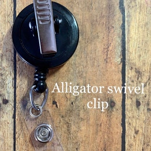 May include: Black retractable badge reel with an alligator swivel clip and a clear plastic strap with a snap closure. The text "Alligator swivel clip" is printed on the image.