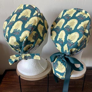 May include: Two green and yellow surgical scrub hats with the text "What Would Dolly Do?" repeated on the fabric. The hats are tied with green ribbon.