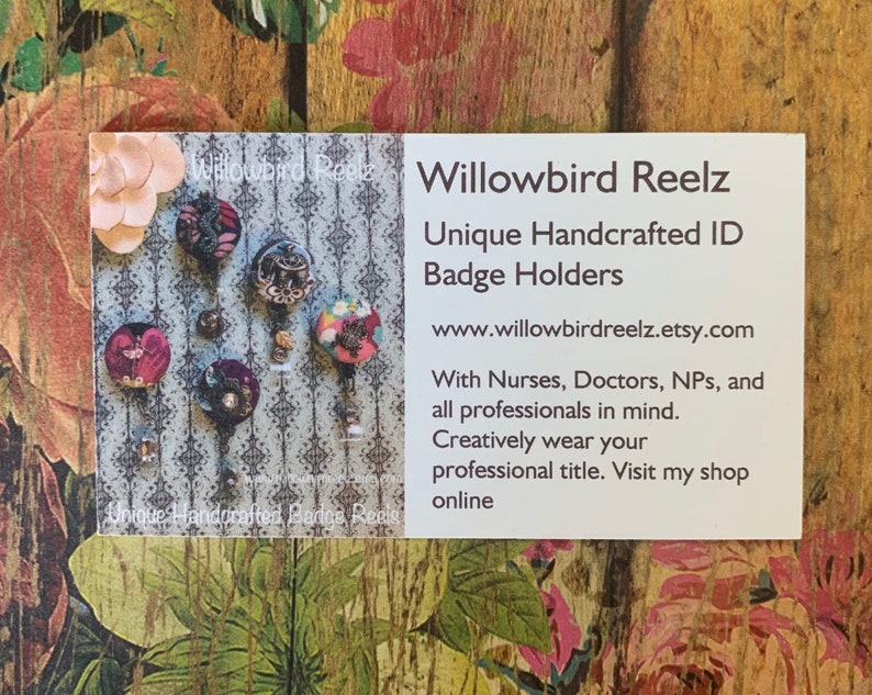 May include: A business card with the text "Willowbird Reelz Unique Handcrafted ID Badge Holders" and a website address. The card displays several unique ID badge holders with decorative designs. The background is a floral pattern.