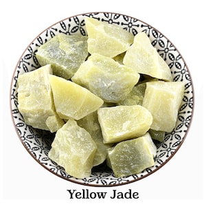 Puede incluir: Un cuenco lleno de piedras de jade amarillo en bruto. El cuenco presenta un patrón geométrico en blanco y negro a lo largo del borde. El texto "Yellow Jade" está impreso en negro debajo del cuenco, identificando el mineral de las piedras.