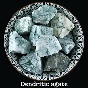 May include: A bowl of dendritic agate stones. The stones are white with green dendrites. The bowl is white with a black and white floral pattern.