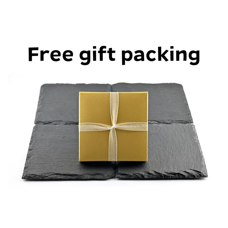 May include: A square gold gift box tied with a thin, translucent ribbon, centered on four dark gray, textured slate coasters arranged in a square formation. The text "Free gift packing" appears in black letters above the items.