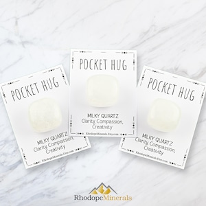 Op de afbeelding: Drie witte pocket hug stenen met de tekst "POCKET HUG" en "MILKY QUARTZ Duidelijkheid, Mededogen, Creativiteit RhodopeMinerals.Etsy.com" op elke kaart.