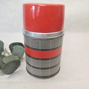 May include: A retro red and silver thermos flask with a black and white striped design. The flask features a red lid and a silver band. The body of the flask has a horizontal red stripe.