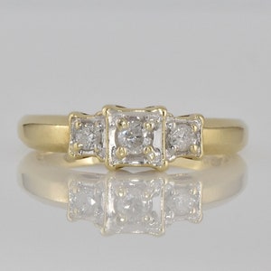 May include: A gold band ring with three square-shaped diamonds set in the center.