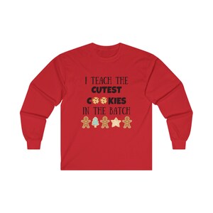 May include: Red long-sleeve t-shirt with the text "I teach the cutest cookies in the batch" and a row of gingerbread cookies, a Christmas tree, and stars.