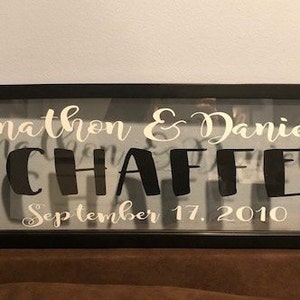 May include: A black framed shadow box with a white inscription that reads "Jonathon & Danielle Schaffer September 17, 2010".