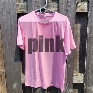 May include: A pink t-shirt with the word "pink" printed in black on the front.