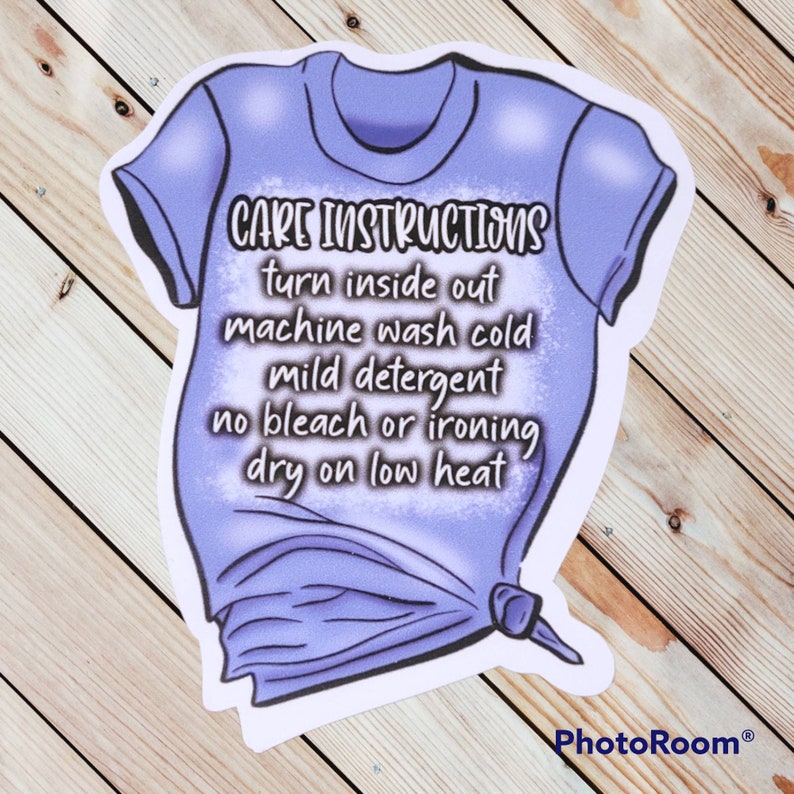 Peut inclure: Un t-shirt violet avec des instructions d'entretien imprim&eacute;es dessus. Les instructions disent : "Retourner &agrave; l'envers, laver en machine &agrave; froid, d&eacute;tergent doux, pas de javel ni de repassage, s&eacute;cher &agrave; basse temp&eacute;rature."