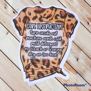 Peut inclure: Un autocollant avec une illustration de dessin anim&eacute; d'un t-shirt &agrave; imprim&eacute; l&eacute;opard avec des instructions d'entretien imprim&eacute;es dessus. Les instructions sont les suivantes : "CARE INSTRUCTIONS turn inside out machine wash cold mild detergent no bleach or ironing dry on low heat"
