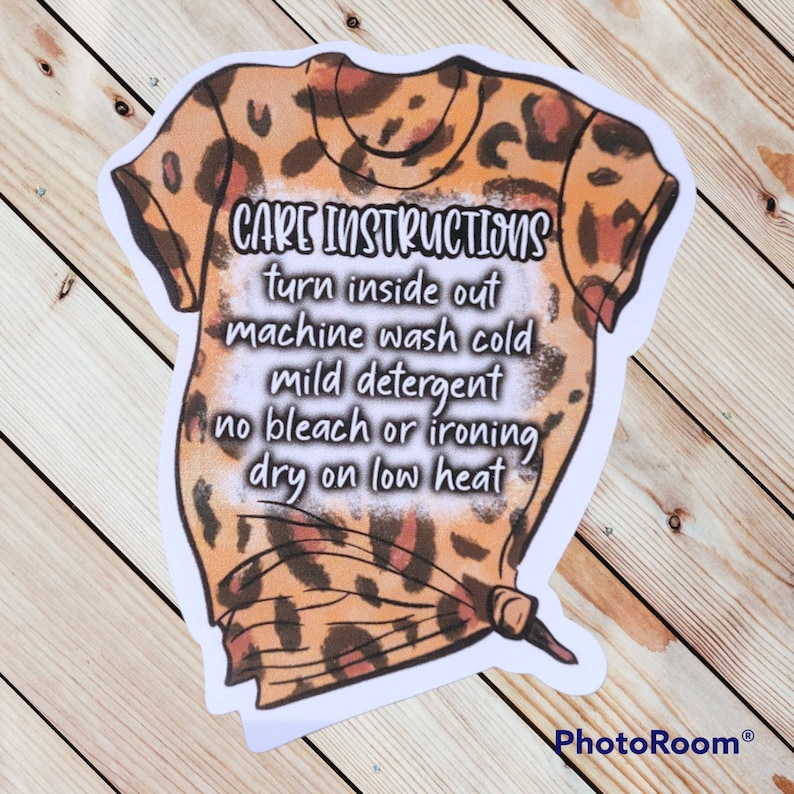 Peut inclure: Un autocollant avec une illustration de dessin anim&eacute; d'un t-shirt &agrave; imprim&eacute; l&eacute;opard avec des instructions d'entretien imprim&eacute;es dessus. Les instructions sont les suivantes : "CARE INSTRUCTIONS turn inside out machine wash cold mild detergent no bleach or ironing dry on low heat"