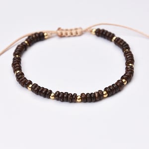 Op de afbeelding: Een bruine houten kralen armband met gouden accenten en een beige koord.