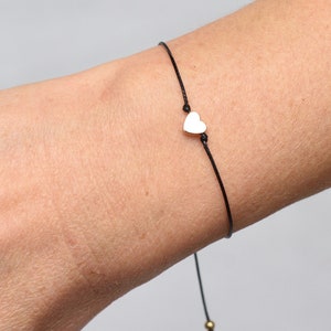 Puede incluir: Un sencillo brazalete de cuerda negra con un pequeño dije de corazón plateado.