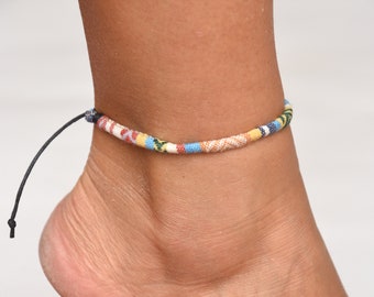 May include: A colorful ankle bracelet with a black cord tie. The bracelet is made of woven fabric with blue, yellow, red, and white stripes.