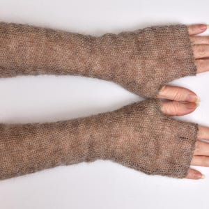 May include: A pair of long, fingerless gloves crafted from a light brown, fuzzy, semi-sheer knit fabric. These arm warmers extend from the knuckles to the mid-forearm, featuring a simple, straight-cut design with an opening for the thumb.