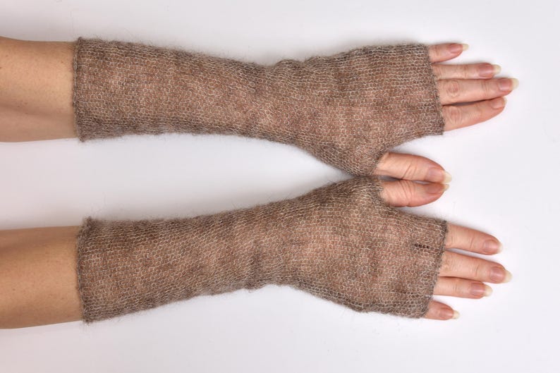 May include: A pair of long, fingerless gloves crafted from a light brown, fuzzy, semi-sheer knit fabric. These arm warmers extend from the knuckles to the mid-forearm, featuring a simple, straight-cut design with an opening for the thumb.