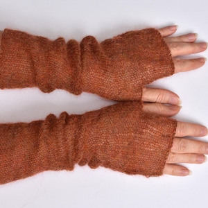 May include: A pair of rust-colored fingerless gloves made from a lightweight, semi-sheer knitted fabric. The gloves feature a textured, loose-knit construction that extends from the knuckles to the mid-forearm, with a simple opening for the thumb.