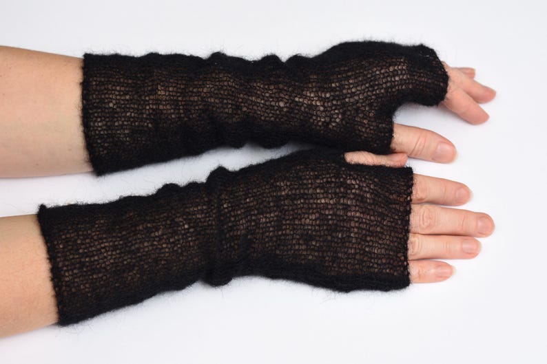 May include: A pair of black fingerless gloves crafted from a fine, sheer, and fuzzy knit material. These arm warmers extend from the knuckles to the mid-forearm, featuring a lightweight, semi-transparent texture with a soft, brushed appearance.
