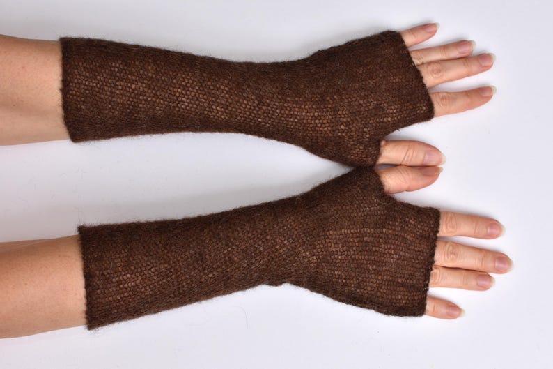 May include: A pair of dark brown fingerless gloves made from a fine, semi-sheer knitted yarn. These arm warmers extend from the knuckles to the mid-forearm, featuring a simple, open-ended design with a dedicated opening for the thumb.