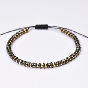 Puede incluir: Un brazalete de cuentas negras y doradas con un cordón negro y cierre ajustable de nudo deslizante.