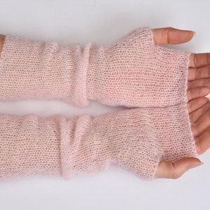 May include: A pair of pale pink fingerless gloves crafted from a fine, sheer, knitted yarn. These arm warmers feature a delicate, open-stitch texture that extends from the knuckles up to the mid-forearm, providing a lightweight layer.