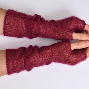May include: A pair of deep magenta fingerless gloves crafted from a fine, sheer knitted yarn. These long, arm-covering accessories feature a loose, airy texture with a distinct thumb opening, extending from the knuckles up to the mid-forearm.