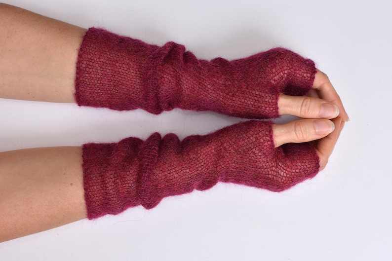 May include: A pair of deep magenta fingerless gloves crafted from a fine, sheer knitted yarn. These long, arm-covering accessories feature a loose, airy texture with a distinct thumb opening, extending from the knuckles up to the mid-forearm.