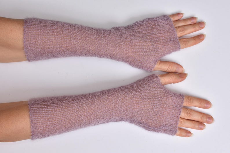 May include: A pair of long, fingerless gloves in a soft, muted mauve color. These arm warmers feature a lightweight, semi-sheer knitted texture that extends from the knuckles up to the mid-forearm, leaving the fingers and thumb exposed.