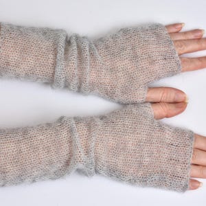 May include: A pair of light gray fingerless gloves crafted from a sheer, fuzzy knit material. These arm warmers feature a loose, open weave texture that extends from the knuckles up to the mid-forearm, providing a lightweight layer of coverage.