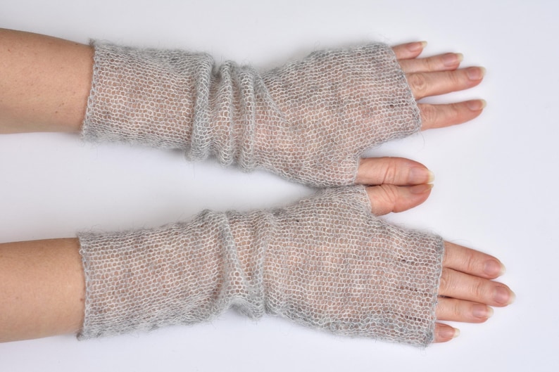 May include: A pair of light gray fingerless gloves crafted from a sheer, fuzzy knit material. These arm warmers feature a loose, open weave texture that extends from the knuckles up to the mid-forearm, providing a lightweight layer of coverage.