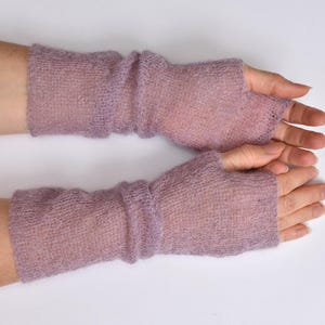 May include: A pair of lavender fingerless gloves crafted from a sheer, lightweight, and fuzzy knit fabric. These arm warmers feature a simple pull-on design that covers the forearm and the back of the hand, leaving the fingers and thumb exposed.