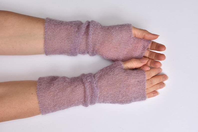 May include: A pair of lavender fingerless gloves crafted from a sheer, lightweight, and fuzzy knit fabric. These arm warmers feature a simple pull-on design that covers the forearm and the back of the hand, leaving the fingers and thumb exposed.