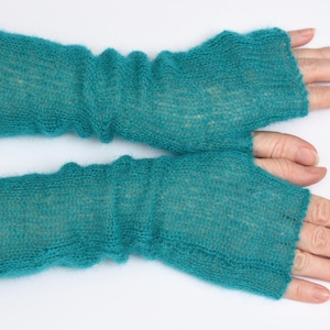 May include: A pair of teal fingerless gloves crafted from a fine, semi-sheer knitted yarn. The gloves feature a ribbed texture with a loose, slightly gathered fit that extends from the knuckles to the mid-forearm, showcasing a soft, fuzzy finish.