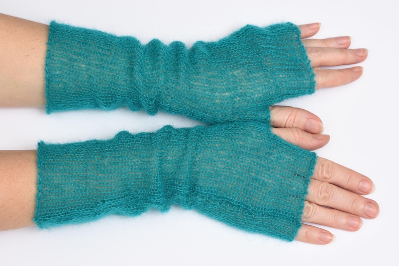 May include: A pair of teal fingerless gloves crafted from a fine, semi-sheer knitted yarn. The gloves feature a ribbed texture with a loose, slightly gathered fit that extends from the knuckles to the mid-forearm, showcasing a soft, fuzzy finish.
