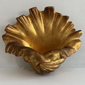 May include: A golden, shell-shaped wall sconce. The decorative piece features a textured, fluted design with a central basin and a twisted, shell-like base. The sconce is finished in a metallic gold.
