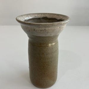 以下が含まれることがあります： 手作りのセラミック花瓶。口が広く、円筒形の胴体。花瓶は主に落ち着いた茶色で、縁は明るく斑点模様です。シンプルで素朴なデザインで、花を飾ったり、装飾品として使用するのに適しています。