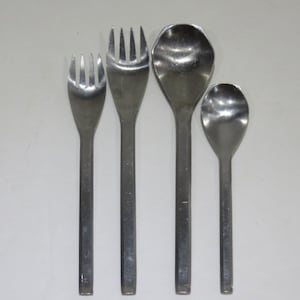 May include: Four pieces of stainless steel flatware are arranged against a white background. The set includes two forks and two spoons. The forks have three and four tines, respectively. The spoons are a serving spoon and a smaller spoon.