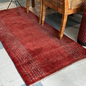 May include: A rectangular red area rug featuring a central solid red field flanked by two vertical borders decorated with a repeating pattern of small, dark, geometric shapes. The rug has a low-pile texture and a finished edge along the sides.