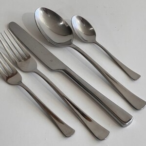 May include: A four-piece stainless steel flatware set consisting of a dinner fork, a salad fork, a dinner knife, and a teaspoon. Each piece features a polished silver finish with a smooth, rounded handle design and a simple, clean aesthetic.
