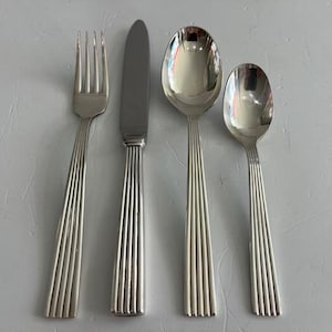 May include: A four-piece stainless steel flatware set consisting of a dinner fork, a dinner knife, a large soup spoon, and a smaller teaspoon. Each piece features a polished silver finish and a distinct vertical ribbed pattern on the handle.