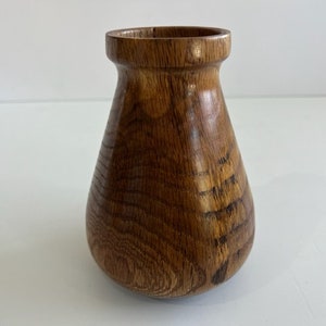 Può includere: Un vaso di legno fatto a mano con un corpo arrotondato e un collo stretto. Il vaso è realizzato in legno marrone caldo, che mostra le naturali venature. Il vaso è un oggetto decorativo.