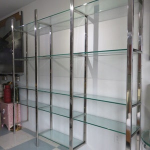 May include: A modern, multi-shelf display unit with a polished chrome frame and clear glass shelves. The unit has a rectangular design and is suitable for displaying items in a home or retail setting. The shelves are evenly spaced and provide ample storage space.