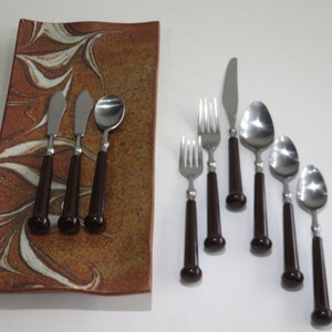 May include: A set of stainless steel silverware with dark brown handles. The set includes forks, knives, and spoons. The silverware is arranged on a rectangular brown and white patterned serving dish.
