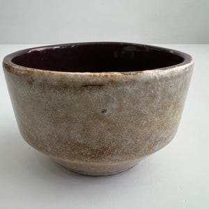 Puede incluir: Un cuenco pequeño de cerámica hecho a mano con forma redondeada. El exterior es de color marrón moteado, mientras que el interior es de color marrón oscuro. El cuenco tiene un borde ligeramente irregular, lo que sugiere un origen artesanal. Adecuado para servir porciones pequeñas.