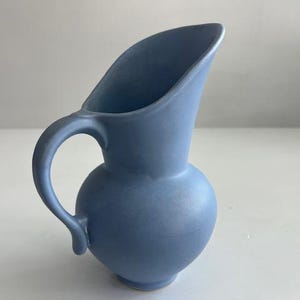 Puede incluir: Jarra de cerámica azul claro con base redondeada y asa curva. La jarra tiene un pico ancho e inclinado. El diseño es sencillo y elegante, adecuado para servir bebidas o como objeto decorativo. Mide aproximadamente 20 cm de alto.