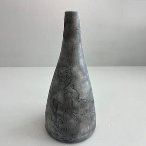 May include: Gray ceramic vase with a slender neck and a wide base. The vase features a hand-drawn design of a deer and foliage. The vase is approximately 10 inches tall.