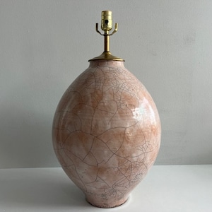 May include: A large, egg-shaped ceramic table lamp with a crackle glaze finish in shades of peach and brown. The lamp has a brass neck and lamp holder. The lamp is a decorative lighting fixture.