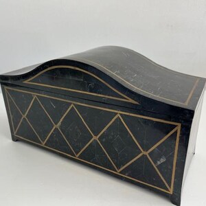 May include: A black decorative box with a curved lid and gold geometric accents. The box has a rectangular shape with a patterned design on the front and sides. The lid is slightly arched, adding a unique touch to the design.