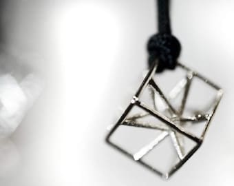 May include: A silver geometric pendant with a cube shape and a black cord.