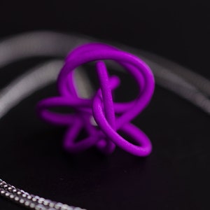 Op de afbeelding: Een paarse 3D-geprinte hanger in de vorm van een knoop, hangend aan een zilveren ketting.